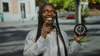 Fototapeta premium Woman with glasses holding clock outdoors on city street expressing various emotions in striped shirt during daytime.