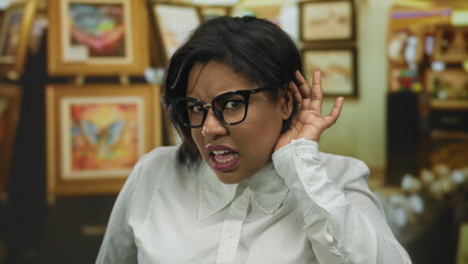 Woman listening intently in art gallery surrounded by colorful paintings wearing glasses and white...
