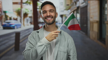Young man smiles holding an italian flag on a city street, capturing a vibrant urban scene outdoors with cultural pride.