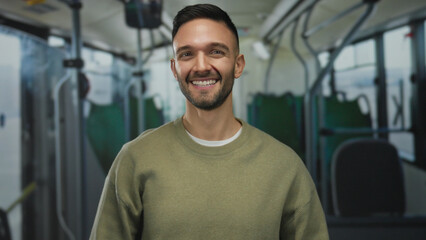 Young hispanic man smiling confidently on a bus while gesturing at his head in a casual sweater showcasing a lively and indoor commuting scene with a cheerful vibe and ambient lighting