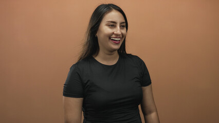 Obraz premium Woman laughing with open mouth and visible teeth in a studio with peach backdrop wearing black shirt; joy confidence.