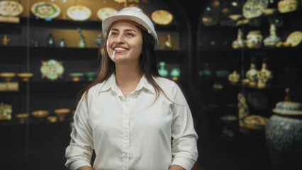 Woman architect wearing a hardhat, smiling and looking up at a museum exhibit in a historic building; curiosity heritage preservation.