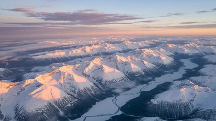 Snow-covered mountains in the early morning light reveal vast landscapes and a winding river in a remote area