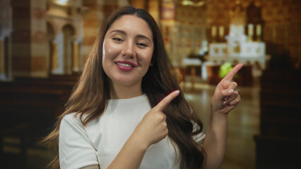 Young hispanic woman smiling and pointing finger at ornate altar in historic church building; spiritual joy inner peace.
