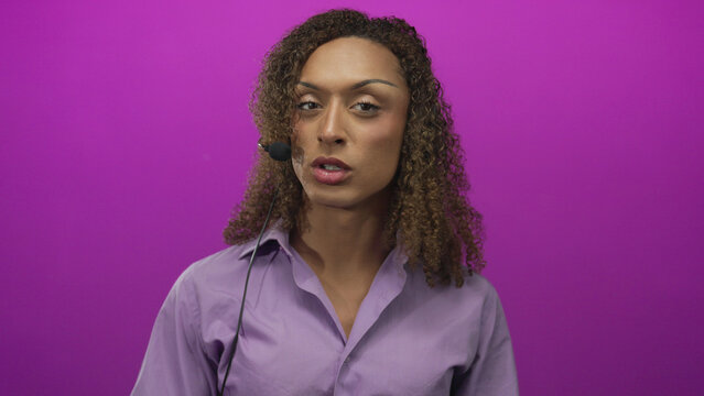 Transgender hispanic woman speaks into headset microphone with animated hand gesture in magenta studio; confidence empowerment.