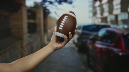 Man holding football on city street with cars and buildings in the background, showcasing a sporting theme in an urban environment with a focus on leisure and sports.