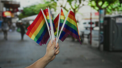 Man holding rainbow flags on a city street, showcasing lgbtq pride with vibrant colors and diverse unity outdoors.