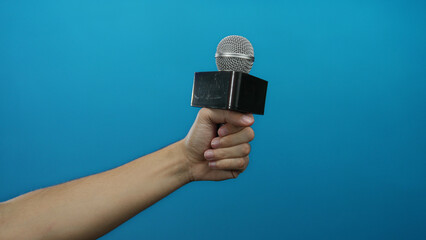 Man holding microphone against blue background, showcasing a presentation or interview setting with...