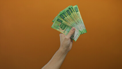 Caucasian man's hand holding russian rubles against an isolated orange wall background, depicting...