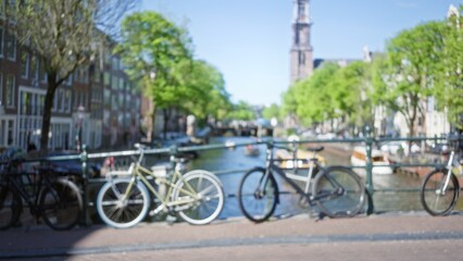 Blurred bicycles against the scenic amsterdam canal backdrop, showcasing the charm of the netherlands with a defocused city view and vibrant bokeh enhancing the urban appeal.