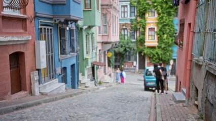 Fototapeta premium Blurred colorful cobblestone street with shallow bokeh, defocused pastel facades, parked car and steps outdoor; background backdrop copyspace overlay.
