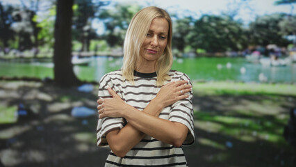 Obraz premium Woman with crossed arms and hands on shoulders, wearing striped shirt and visible ring, pensive expression in studio; sadness reflection.