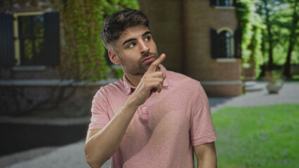 Hispanic man pointing finger to building entrance and showing thumbs up with thoughtful expression; approval.