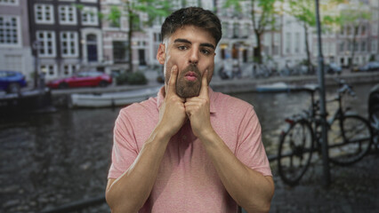 Man points finger toward camera while standing by the canal street lined with bicycles and historic buildings; curiosity focus.