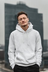 Casual Urban Fashion: Man in White Hoodie Poses Against City Skyscraper Backdrop