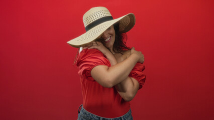 Woman hugging herself with arms crossed showing bare shoulders in a red studio; self love confidence joy.