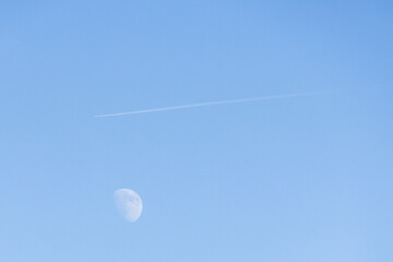 Jet contrail flying past moon in clear blue sky