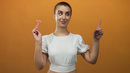 Woman with short buzzcut holding a pink razor and pointing index finger while smiling in studio...