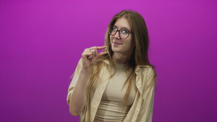 Young blonde woman wearing glasses pinches fingertips to show tiny measure in purple studio;...
