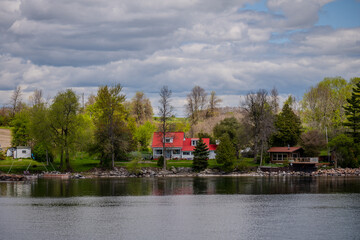 Red roof house and lakeside cabins among trees by calm water