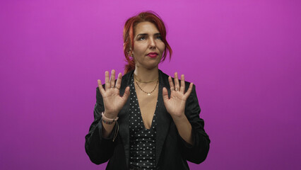 Woman with hands raised, palms forward and fingers splayed in studio against magenta wall in black blazer and polka dots; hesitation.