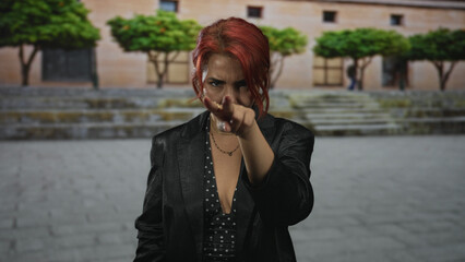 Woman pinches nose with hand on urban street steps wearing polka dot dress and black blazer;...