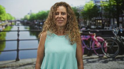 Woman with closed eyes and bare arms beside a pink bicycle on a street canal bridge wearing a turquoise top; serenity reflection.