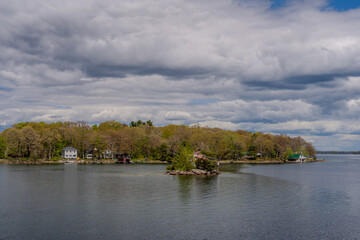 Obraz premium Small wooded island and lakeside cottages under cloudy sky