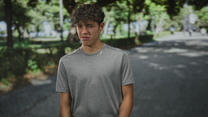 Fototapeta premium Teen boy grimacing with hand held out and silver chain visible, wearing gray tshirt on a street; disgust.
