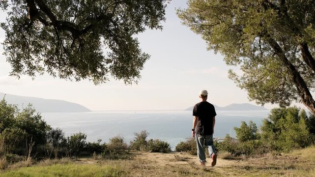 Vlora, Albania - December 28, 2025: A young man walks toward the edge of a coastal hill and looks at the sea view. Calm everyday moment in a natural landscape.