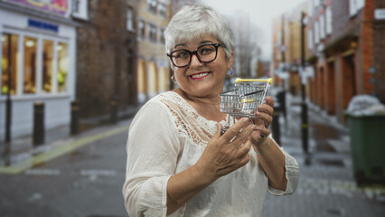 Woman holding miniature shopping cart with hands, smiling and looking at tiny trolley on a shopping...