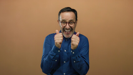Hispanic man expressing joy isolated over a brown background with hands clapping and smiling,...
