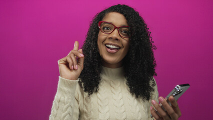 Woman scratches head holding smartphone in studio setting with bright pink backdrop while frowning at the screen; confusion.