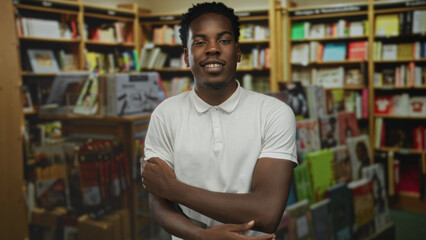 Man face smiling arms crossed wearing white polo shirt standing amid bookshelves in library  confidence focus. © Krakenimages.com