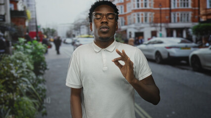 Young african american man in white polo shirt gestures ok sign with hand in busy city street; approval.