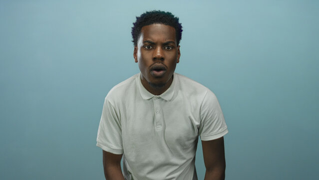 Young african american man with open mouth and raised eyebrows in studio wearing white polo shirt looking forward; surprise.