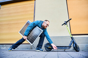 Man connects solar panel to electric scooter for charge, highlighting practical application of sustainable renewable energy. Concept of integration of eco-friendly technology in urban transportation.