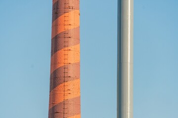 Striking juxtaposition of two weathered chimneys, one red and white striped, the other brown and...