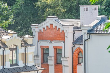 Row of old European red brick buildings with white decorative details and pitched roofs, outdoor setting, multiple windows some arched or ornamental, natural daytime lighting, trees in background,