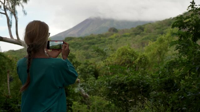 Mature woman hikes in Charco Verde park on Ometepe Island while taking photos of the surrounding jungle and volcano.