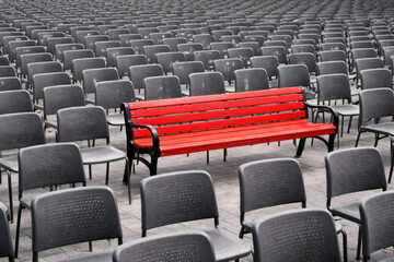 A red bench among many gray chairs.