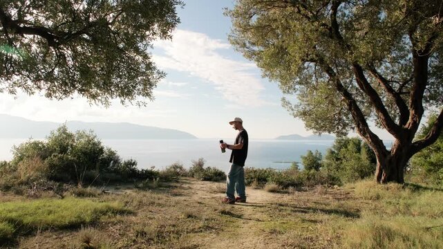 Vlora, Albania - December 28, 2025: A young man drinks water on a coastal hill among trees with a sea view in the background. Everyday outdoor moment.