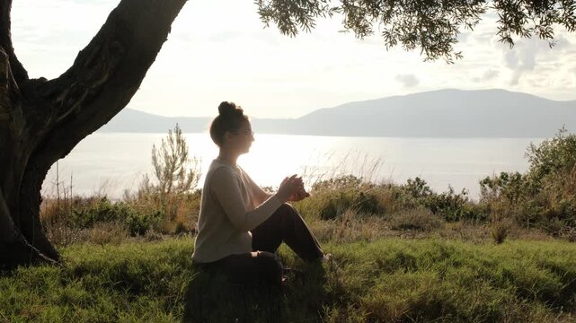 Woman shuffling tarot cards and looking at a card outdoors with sea view at sunset. Spiritual lifestyle, intuition, mindfulness, calm atmosphere and self reflection concept.