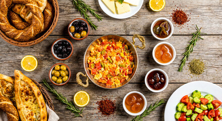 Turkish breakfast spread with menemen scrambled eggs olives cheese and simit bread on a rustic wooden table.