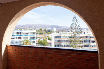 Photograph taken through shaped window, semi-circular one, which frames a view of modern high-rise buildings. A red brick wall section Outside features multi-story buildings with numerous windows.