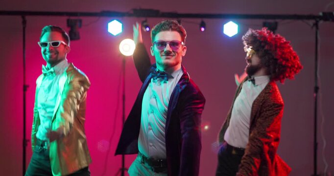 Dancers group dance party disco nightlife. Men in retro suits dance beneath vibrant stage lights, a cheerful celebration showcasing confident performance with smiles. Concept of party dance fun.