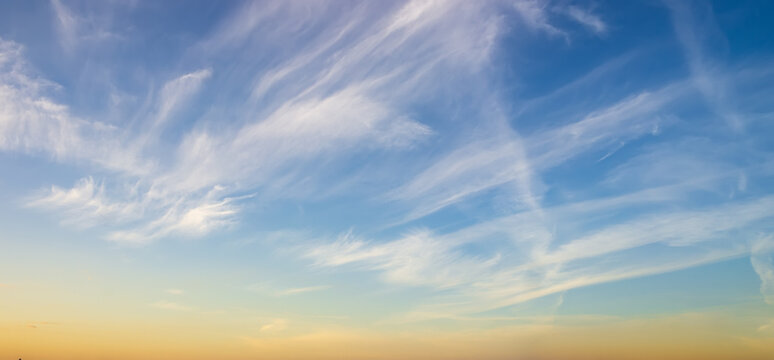 Wispy cirrus clouds streak across a vast blue sky, softly lit by warm golden hour sunlight near the horizon, creating a serene, expansive, tranquil atmosphere