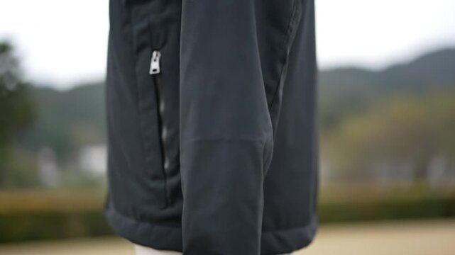 A focused close-up shot highlights the durable fabric and intricate details of a stylish dark-colored jacket, featuring a prominent metallic zipper on the side. The background is softly blurred, creat