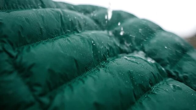 A highly detailed, macro close-up shot captures the rich texture of a deep green, water-resistant fabric, likely from durable outdoor apparel such as a quilted jacket. Tiny water droplets are visible 