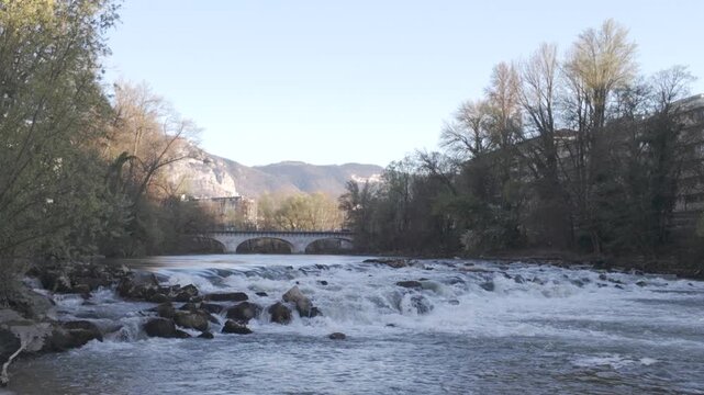 Spring rapids and small waterfalls on Arve River with arched bridge and fresh foliage